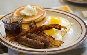 팬케이크, 메이플 시럽, 소시지, 베이컨 스트립, 계란 프라이가 있는 미국식 아침 식사